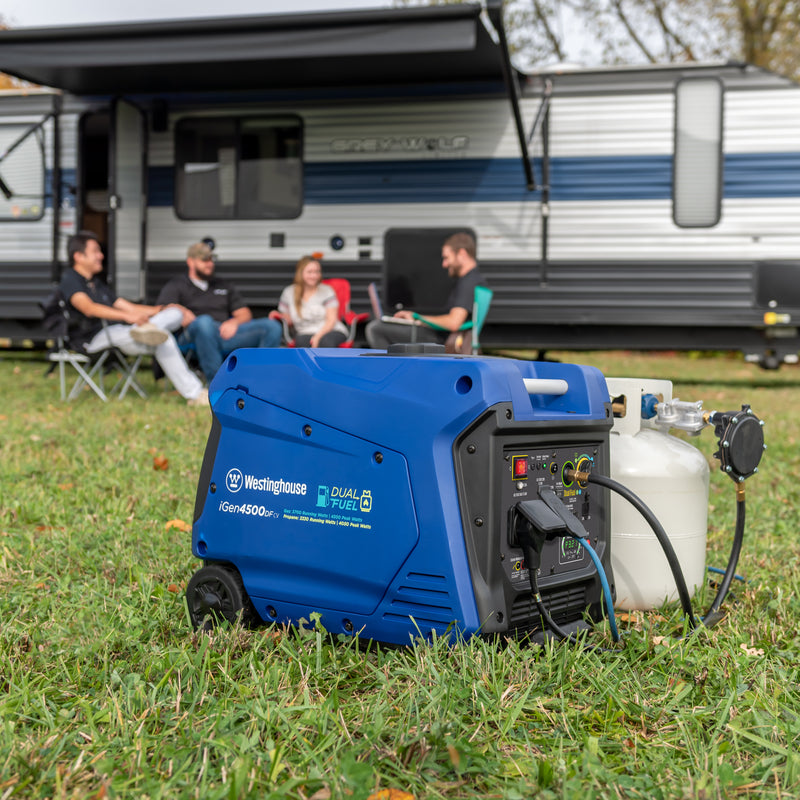 Westinghouse | iGen4500DFcv dual fuel portable inverter generator with co sensor shown sitting in the grass with a propane tank hooked up to it with a camper and people sitting in lawn chairs in the background