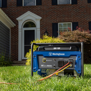 Westinghouse | WGen3600v portable generator sitting in the grass with two cords plugged in. A brick house is in the background.