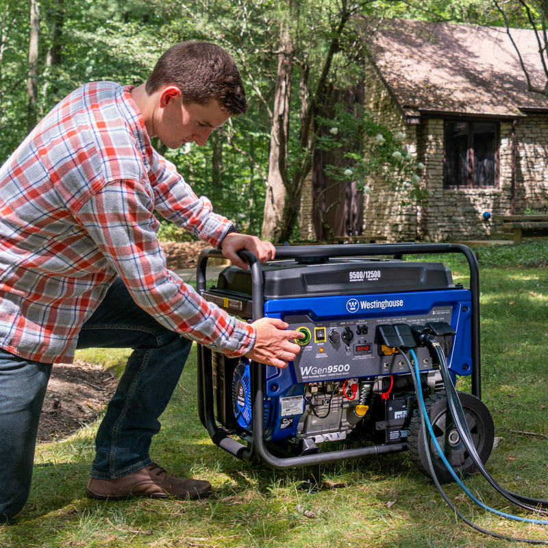 Westinghouse | WGen9500 portable generator sitting in grass with trees and house in the background. A man is kneeling next to the generator and pressing the electric start button.