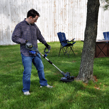 A man cuts the grass around the bottom of a tree using a string trimmer