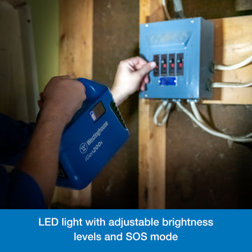 Westinghouse | iGen200s Portable Power Station flashlight feature being used to illuminate a box of circuit breakers. A blue banner along the bottom reads, "LED light with adjustable brightness levels and SOS mode".