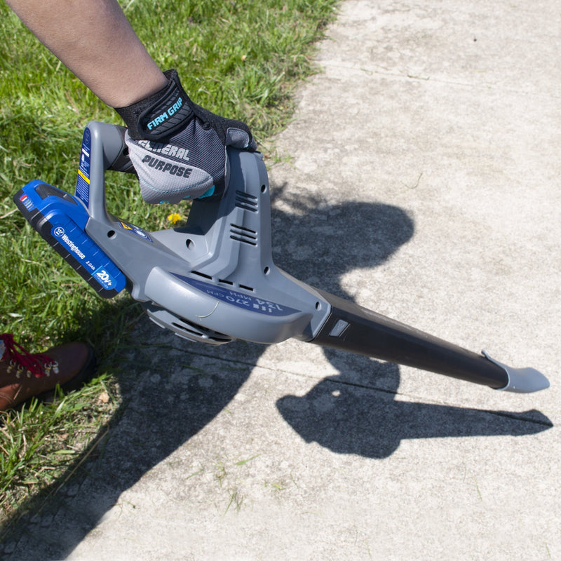 A hand holding a leaf blower on a background of sidewalk and grass