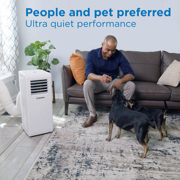 Westinghouse | WPac10000 Portable Air Conditioner shown in use in a living room with a man sitting on a couch petting his dogs with words at the top of the image reading - people and pet preferred ultra quiet performance