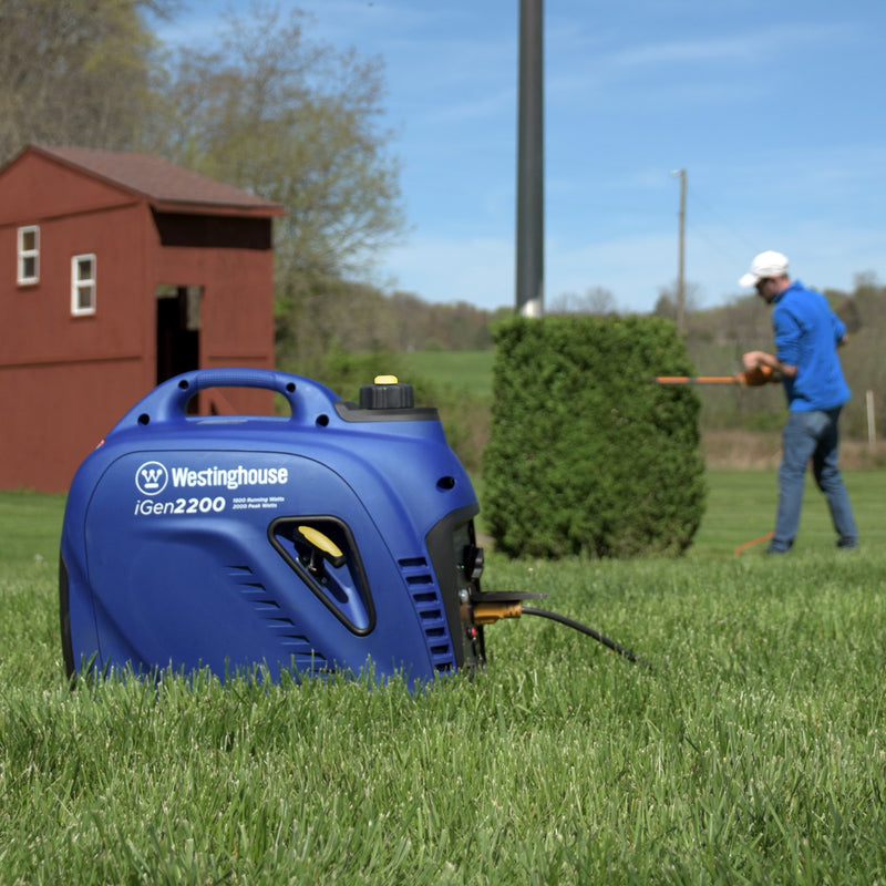 Westinghouse | iGen2200 inverter generator sitting in grass while man works in the background.