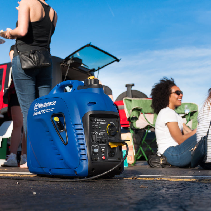 Westinghouse | iGen2200 inverter generator sitting on ground with people tailgating in the background.