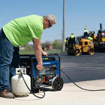 Westinghouse | WGen7500DF portable generator sitting on sidewalk hooked up to propane tank while man uses control panel.