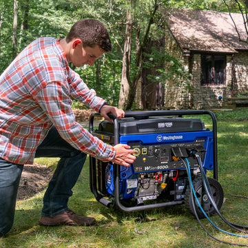 Westinghouse | WGen9500c portable generator sitting in grass with trees and house in the background. A man is kneeling next to the generator and pressing the electric start button.