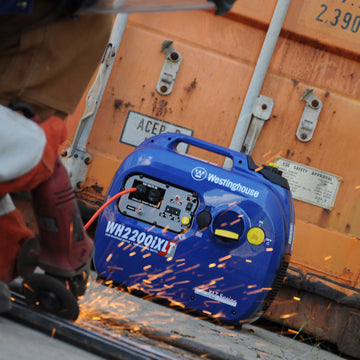 Westinghouse | WH2200iXLT inverter generator with shipping container in the background and someone using an angle grinder in the foreground.